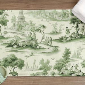 May include: A green and white bath mat with a toile pattern featuring a repeating design of trees, buildings, and people. The pattern is on a white background with green accents.
