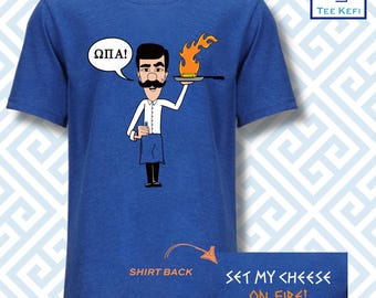 May include: A blue t-shirt with a cartoon illustration of a man holding a pan with a flaming piece of cheese. The text "ΩΠΑ!" is in a speech bubble above the man's head. The text "SET MY CHEESE ON FIRE!" is on the back of the shirt.