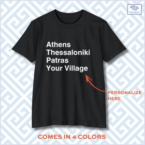 Peut inclure: Un t-shirt noir à manches courtes avec le texte blanc Athens, Thessaloniki, Patras, Your Village. Une flèche orange pointe vers le texte avec la mention PERSONALIZE HERE, et le texte en bas indique COMES IN 4 COLORS.