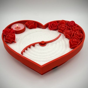 May include: Red heart-shaped sand tray with a white sand design and a small candle in the centre. The tray is decorated with red roses around the edge.