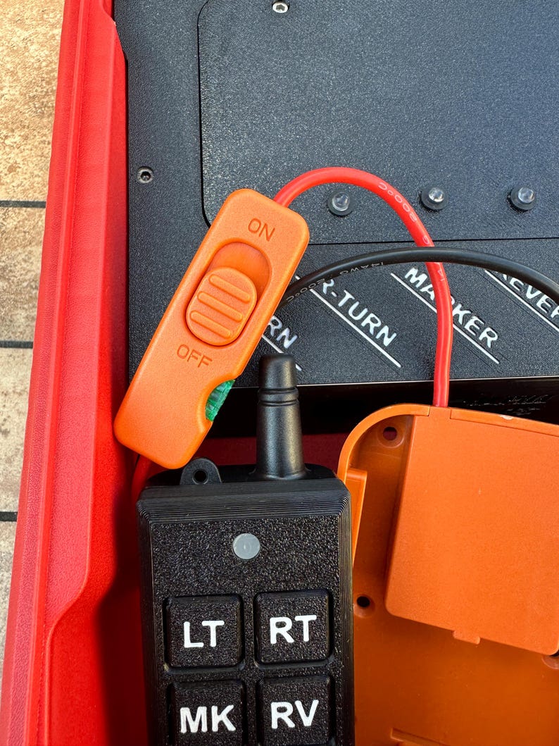May include: An orange switch labeled "ON" and "OFF" is connected to a black control panel with buttons labeled "LT", "RT", "MK", and "RV". A red wire and black cable are also connected to the panel.