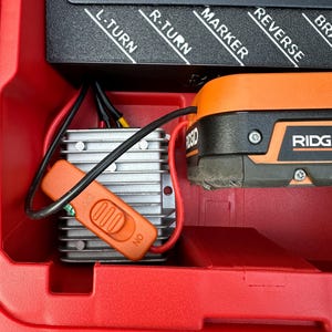 May include: A red Packout modular storage system with a black control panel labeled L-TURN, R-TURN, MARKER, and REVERSE. An orange switch is labeled OFF and ON. A silver component and an orange Ridgid tool are also visible.