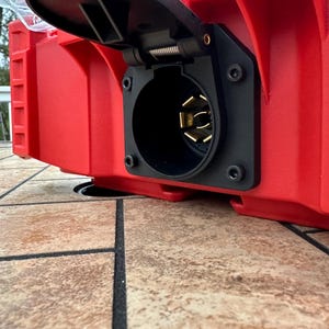 Pu&ograve; includere: Primo piano di un componente elettrico rosso e rettangolare con una presa nera e circolare. La presa ha dei pin dorati ed &egrave; montata su una superficie rossa. Il componente fa probabilmente parte di un sistema elettrico.
