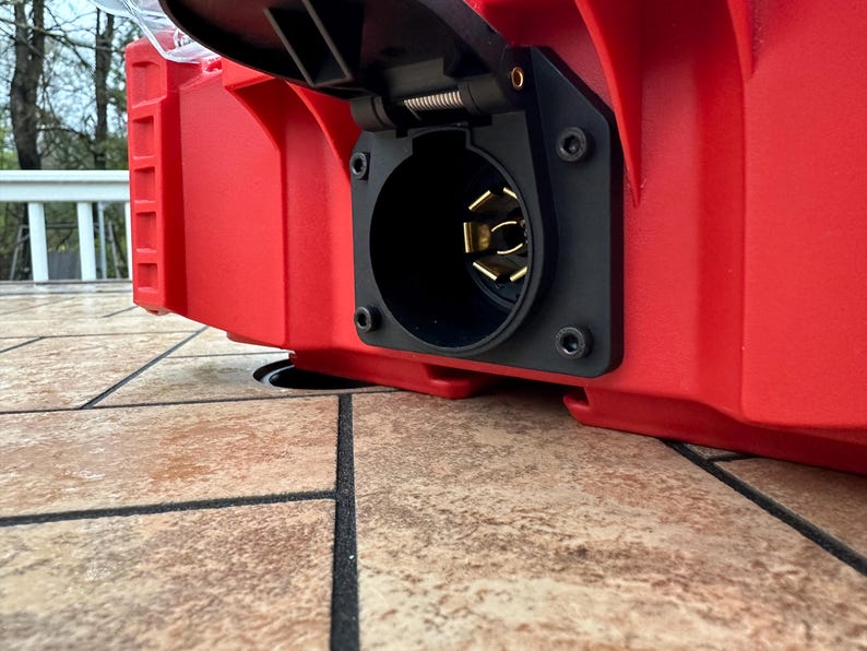 Pu&ograve; includere: Primo piano di un componente elettrico rosso e rettangolare con una presa nera e circolare. La presa ha dei pin dorati ed &egrave; montata su una superficie rossa. Il componente fa probabilmente parte di un sistema elettrico.