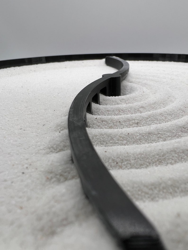 May include: A black plastic border curves around a white sand surface, creating a zen garden design.
