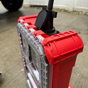 Pu&ograve; includere: Un organizer per utensili in plastica rossa e trasparente con un cavo di alimentazione e una spina neri collegati. L'organizer ha un coperchio trasparente e chiusure e dettagli rossi. L'immagine &egrave; stata scattata all'aperto.