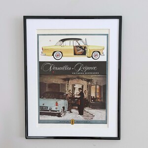 May include: Framed vintage advertisement featuring two classic cars. The top car is yellow with a black roof, the bottom car is light blue. The advertisement includes the text "Versailles et Régence" and "Voitures Heureuses".