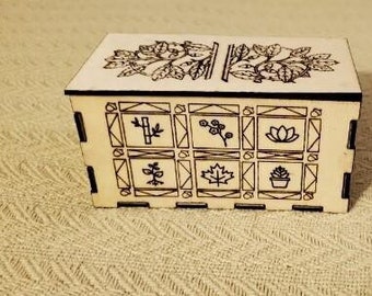 Op de afbeelding: Een houten doos met een decoratief ontwerp met een boom en verschillende plantenmotieven. De doos heeft een scharnierend deksel en is gemaakt van licht hout.