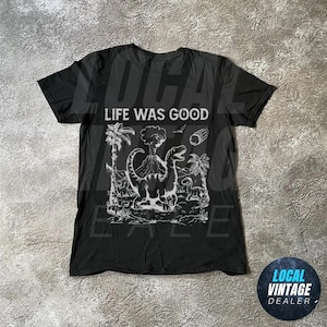 Könnte beinhalten: Schwarzes T-Shirt mit einem weißen Grafikdruck von Dinosauriern und einem Vulkan. Der Text "Life Was Good" ist auf dem Shirt gedruckt.