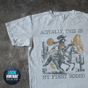 Koszulka Western Cowboy Raccoon – „Właściwie to moje pierwsze rodeo” Zabawna koszulka graficzna, estetyka vintage country, koszulka Y2K Rodeo