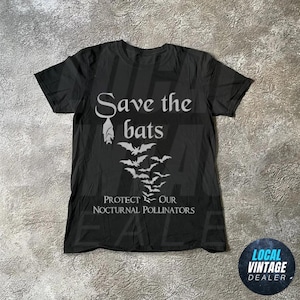 May include: Black t-shirt featuring white text and bat illustrations. The shirt displays the words "Save the bats" and "Protect our nocturnal pollinators". A vintage dealer logo is visible in the bottom right corner.
