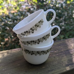 May include: Stack of three white ceramic mugs with a black floral pattern around the rim.