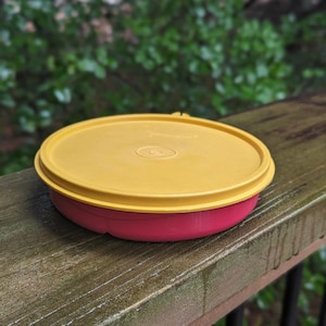 May include: A yellow plastic container with a red lid. The container is sitting on a wooden surface.