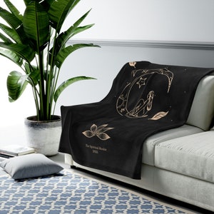 May include: Black fleece throw blanket with a gold design of a woman sitting on a crescent moon with stars and leaves. The text "The Spiritual Rookie 2021" is printed in gold at the bottom of the blanket.