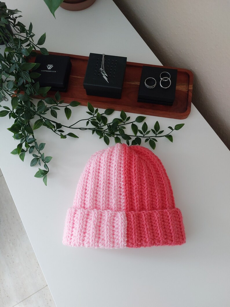May include: A pink and coral knitted beanie hat. The hat is made of soft yarn and has a ribbed texture.
