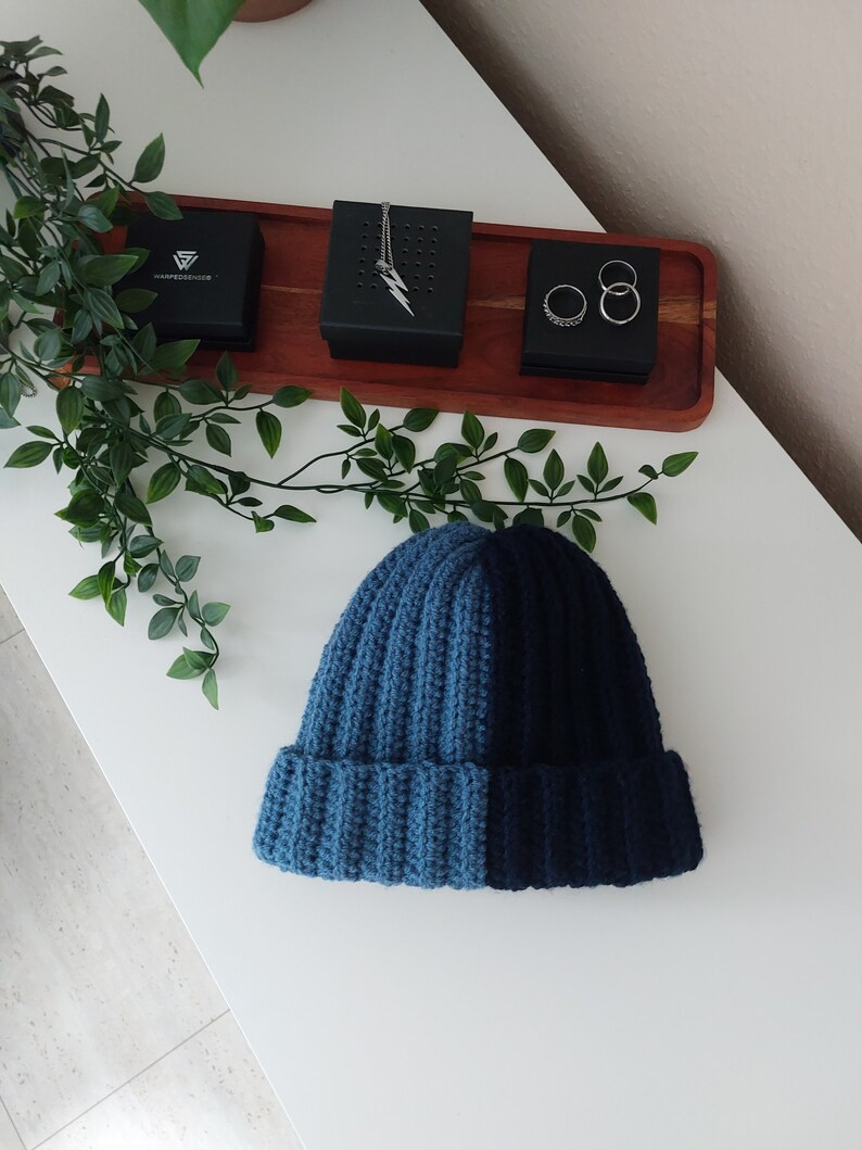 May include: A blue and dark blue knitted beanie hat with a ribbed texture.