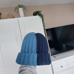 May include: A blue and navy blue knitted beanie hat. The hat is crocheted and has a ribbed texture.