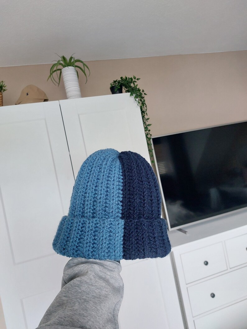 May include: A blue and navy blue knitted beanie hat. The hat is crocheted and has a ribbed texture.