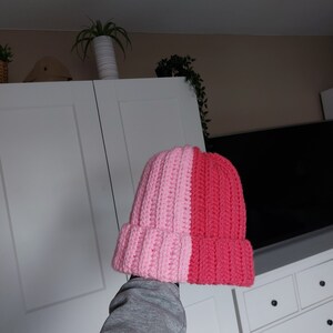 May include: A pink and red crocheted beanie hat. The hat is split down the middle, with one side pink and the other side red.