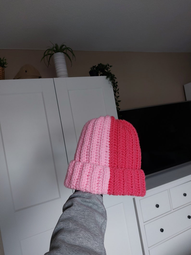 May include: A pink and red crocheted beanie hat. The hat is split down the middle, with one side pink and the other side red.