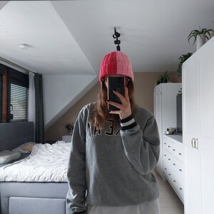 May include: A person wearing a gray sweatshirt with black and white stripes on the cuffs, black leggings, and a pink and red knit beanie. The beanie has a vertical stripe down the center.
