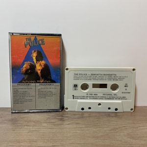 May include: A vintage cassette tape of The Police's album "Zenyatta Mondatta." The cassette case features a colorful design with the band's name and album title. The white cassette tape has the album title and song list printed on it.