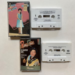 May include: Three cassette tapes featuring Patsy Cline. The first tape is white with black text and says "Patsy Cline Live at the Opry". The second tape is black with a colorful image of Patsy Cline and says "Patsy Cline 12 Greatest Hits". The third tape is white with black text and says "Patsy Cline's Greatest Hits".