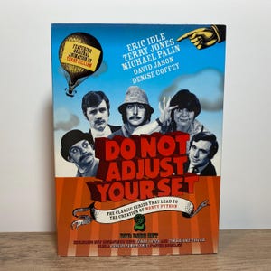 May include: A DVD box set titled Do Not Adjust Your Set featuring a blue sky background with a hot air balloon, a pointing hand, and portraits of five cast members. The text includes names of the actors and the phrase The classic series that lead to the creation of Monty Python.