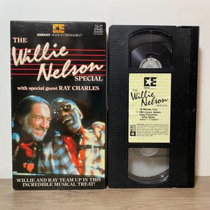 May include: A VHS tape and its case for "The Willie Nelson Special" featuring Ray Charles. The case is black with red and white text, and images of Willie Nelson and Ray Charles. The VHS tape is black with a white label.