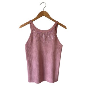 Könnte beinhalten: Ein staubrosa geripptes Strick-Tanktop mit Rundhalsausschnitt und Trägern. Der Ausschnitt ist mit kleinen, irisierenden Pailletten und Perlen verziert. Das Top hängt an einem Holzbügel vor weißem Hintergrund.