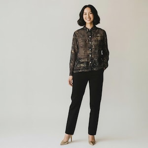 May include: A person wearing a sheer, button-down blouse with a dark, ornate pattern, paired with black trousers and gold heels. The blouse features a detailed design in shades of gold and black.