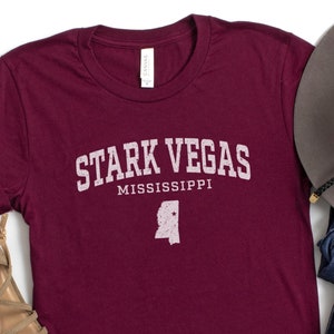 May include: A maroon t-shirt with the text "Stark Vegas Mississippi" and an outline of the state of Mississippi. The shirt is on a white background.