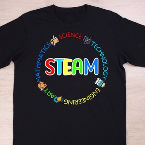 May include: Black t-shirt with a colorful STEAM design. The word "STEAM" is in large, multi-colored letters. The design includes the words "Science, Technology, Engineering, Art, Mathematics" around the word STEAM, with related icons.