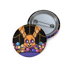 May include: Two round pinback buttons. One button features an orange rabbit character with purple eyes and a white star design, surrounded by colorful balls. The other button is silver with a pin.
