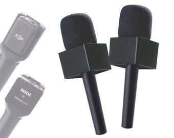 May include: Two black wireless microphones with foam windshields and a black square-shaped mount. The microphones are on a white background.