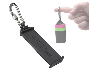 May include: A black keychain with a carabiner clip and a black plastic holder with the text "GRAVITY" embossed on it. The keychain is attached to a small, multi-coloured, plastic object.