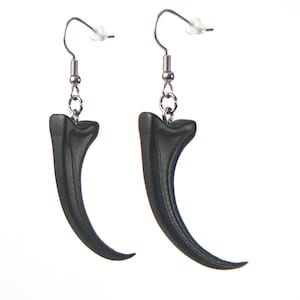 May include: A pair of black claw-shaped earrings with silver hooks. The earrings are made of a smooth, matte material and have a slightly curved shape.