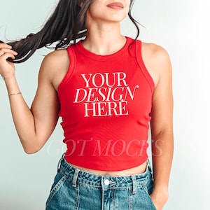 Puede incluir: Un top de tirantes rojo de canalé con el texto "YOUR DESIGN HERE" en blanco. El top es corto y tiene un estilo de espalda nadadora.