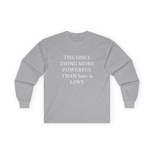 May include: A heather gray long-sleeve shirt with the text "THE ONLY THING MORE POWERFUL THAN hate IS LOVE" in white. The shirt has a crew neck and long sleeves, suitable for cooler weather.
