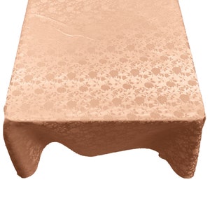 May include: A peach-colored rectangular tablecloth with a floral pattern. The fabric has a subtle sheen and drapes over the edges, showcasing the detailed rose design. The tablecloth is suitable for various events.