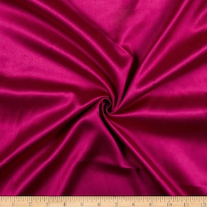 May include: A close-up of a deep pink satin fabric with a smooth, silky texture. The fabric is draped and folded, creating soft curves and folds.