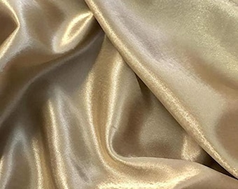 May include: A close-up of a smooth, silky fabric in a light gold color. The fabric is draped and folded, showcasing its luxurious texture.