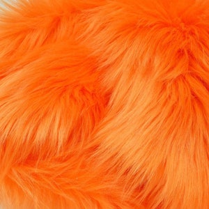 Può includere: Primo piano di un tessuto in pelliccia sintetica di colore arancione brillante. La pelliccia è morbida e soffice, con un aspetto leggermente strutturato.