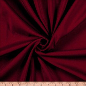 May include: A close-up of a deep red fabric with a subtle textured pattern. The fabric is folded and draped, showcasing its soft and smooth texture.