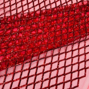 Puede incluir: Tela de lentejuelas roja con un patrón de diamante. Las lentejuelas son pequeñas y están muy juntas, creando un efecto brillante.