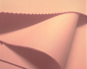Puede incluir: Primer plano de una tela suave de color melocotón doblada en capas. La tela tiene una superficie lisa y ligeramente texturizada.