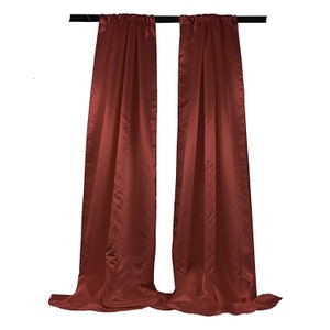 May include: A pair of rust-colored curtains hanging from a black curtain rod. The curtains are made of a smooth, silky fabric.