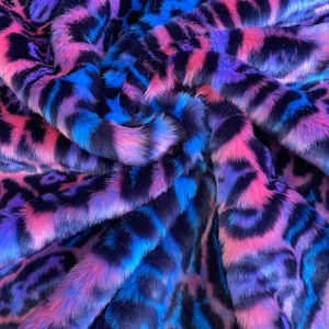 Könnte beinhalten: Ein lebendiger Kunstfellstoff mit einem auffälligen Tiermuster. Das Plüschmaterial weist eine Mischung aus rosa, blauen und violetten Farbtönen auf, die ein auffälliges Muster erzeugen. Die Textur des Stoffes ist weich und einladend, ideal für verschiedene Bastelprojekte.
