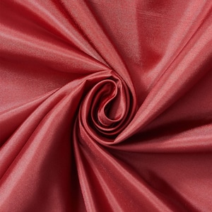May include: Close-up of a swirled, textured fabric in a deep red-brown color. The fabric has a satin sheen, with folds and shadows creating depth. The material appears soft and flowing, suitable for apparel or home decor.