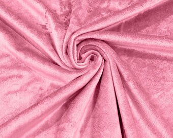 May include: A soft, pink plush fabric with a smooth, velvety texture. The fabric is folded and draped, creating a swirling pattern.